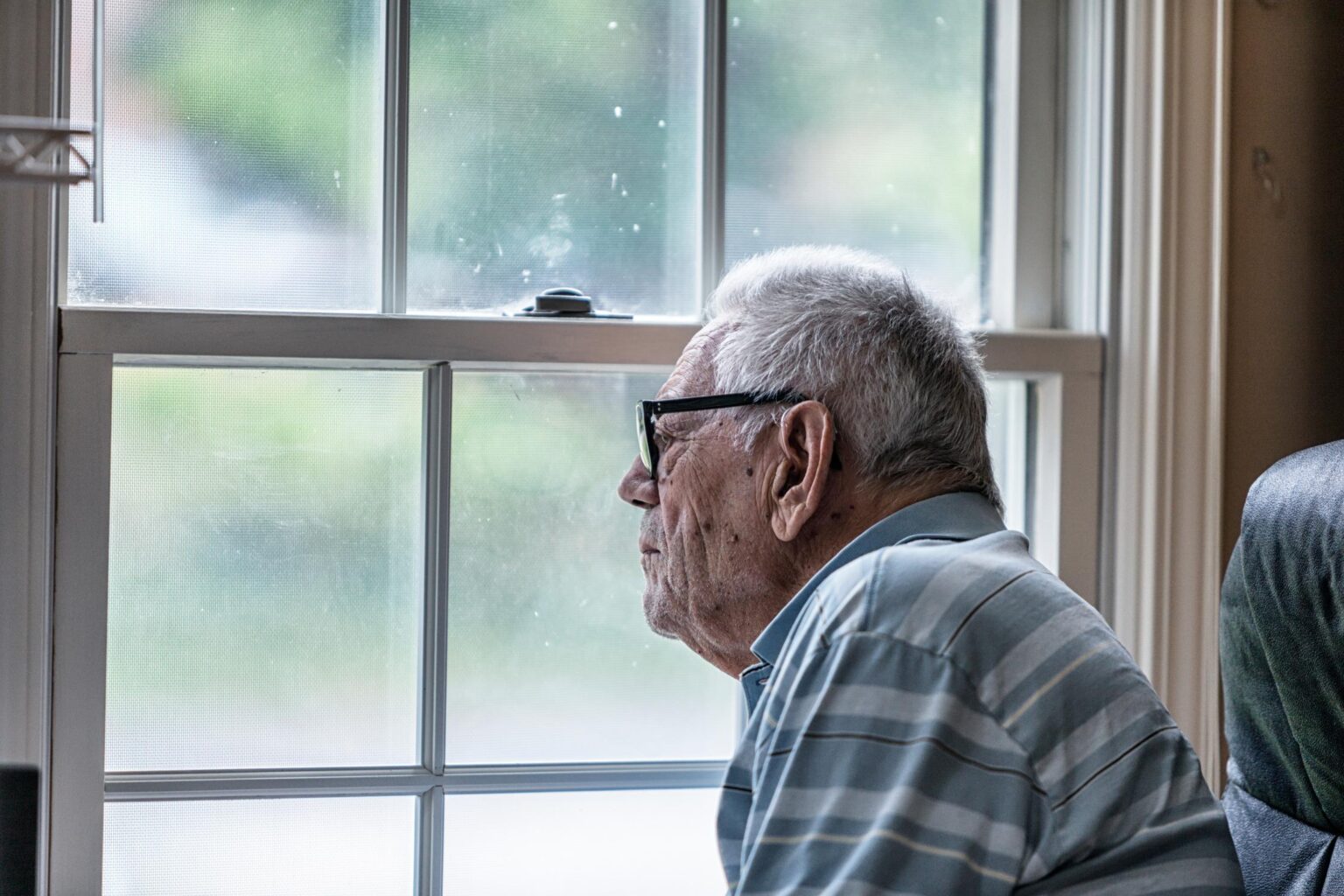 gray haired man with glasses looks out of a window